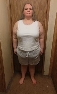 Sarah standing in front of a door wearing shorts and a tank top